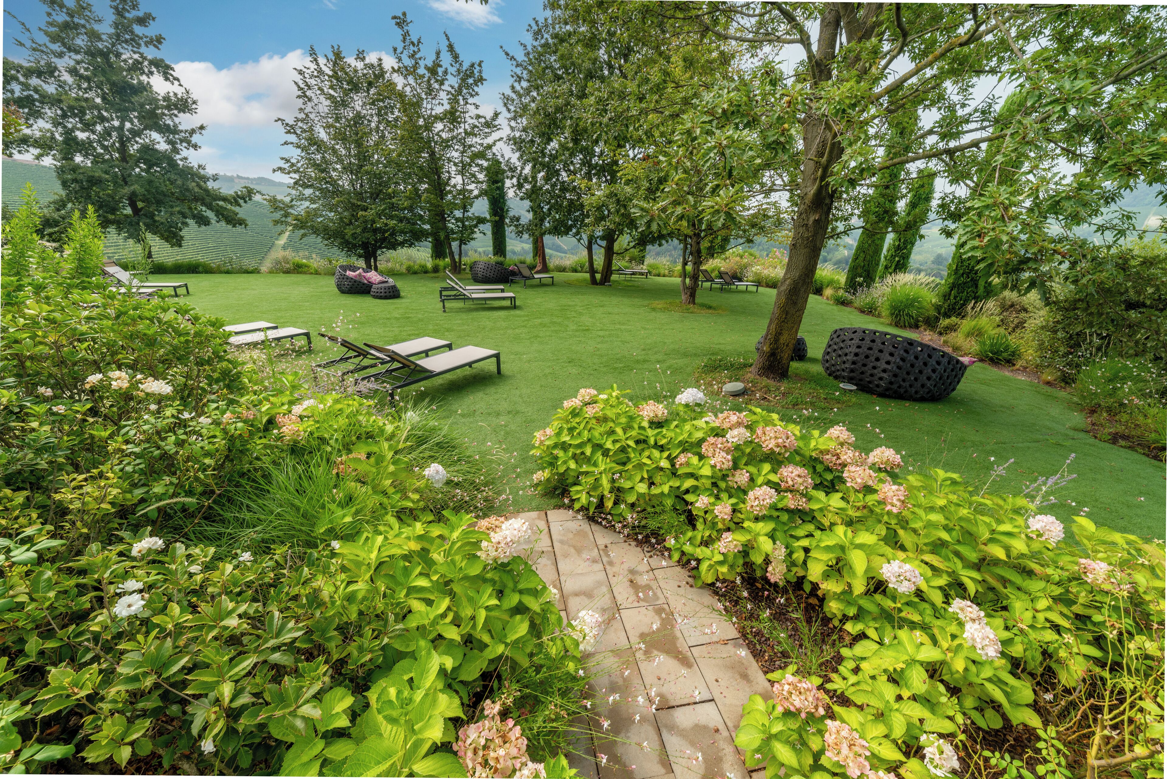 Un jardin bien entretenu, avec une pelouse, des espaces aménagés pour s’asseoir et un chemin.