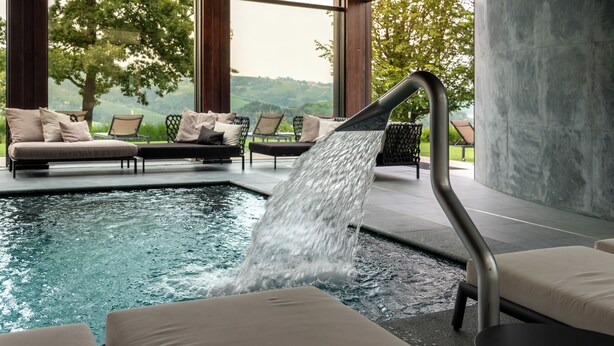 A pool area with a water feature, lounge chairs, and a view of the landscape. - Il Boscareto Resort & Spa (Serralunga d'Alba)