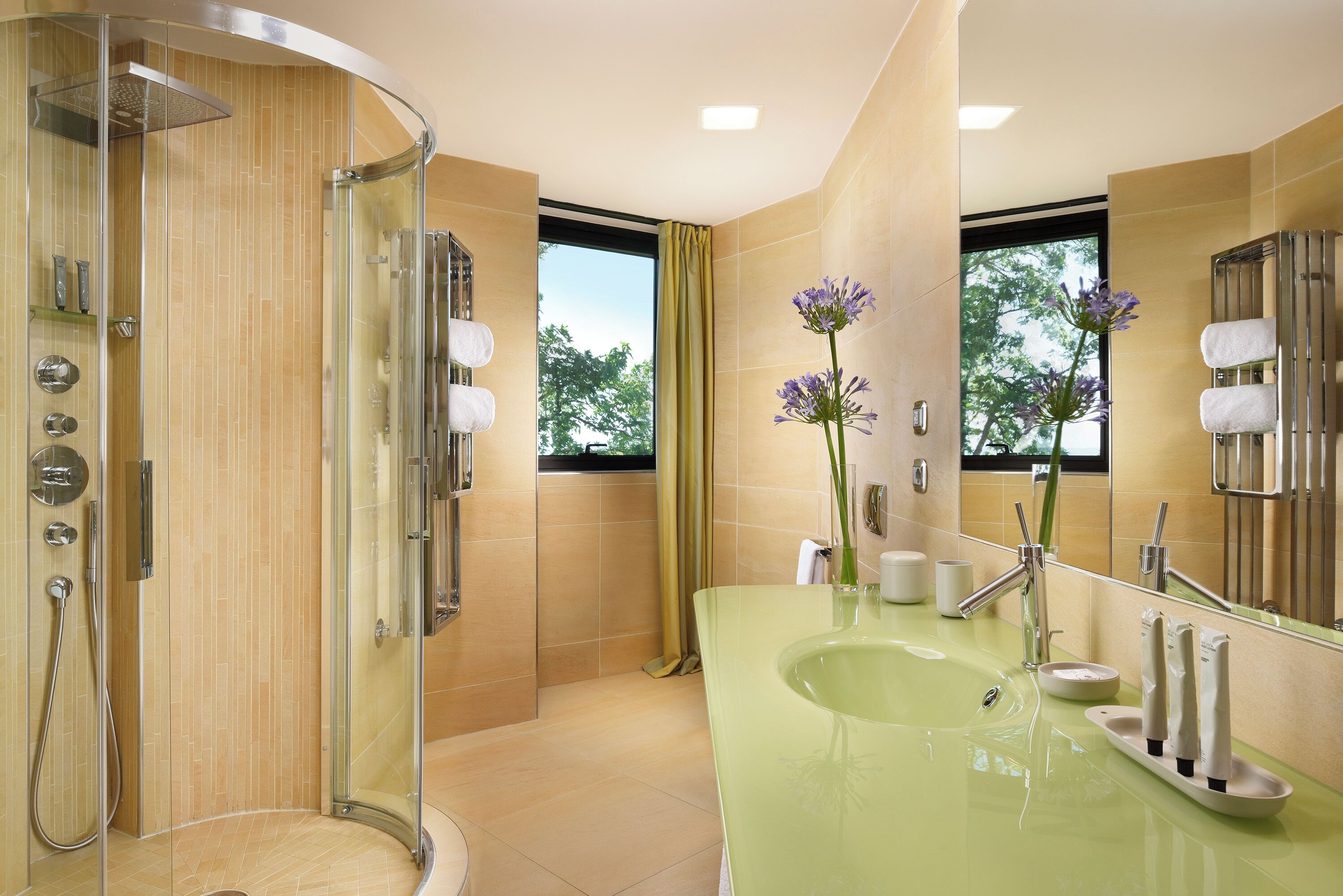 Un baño moderno con ducha de vidrio, un lavamanos verde y un espejo grande.