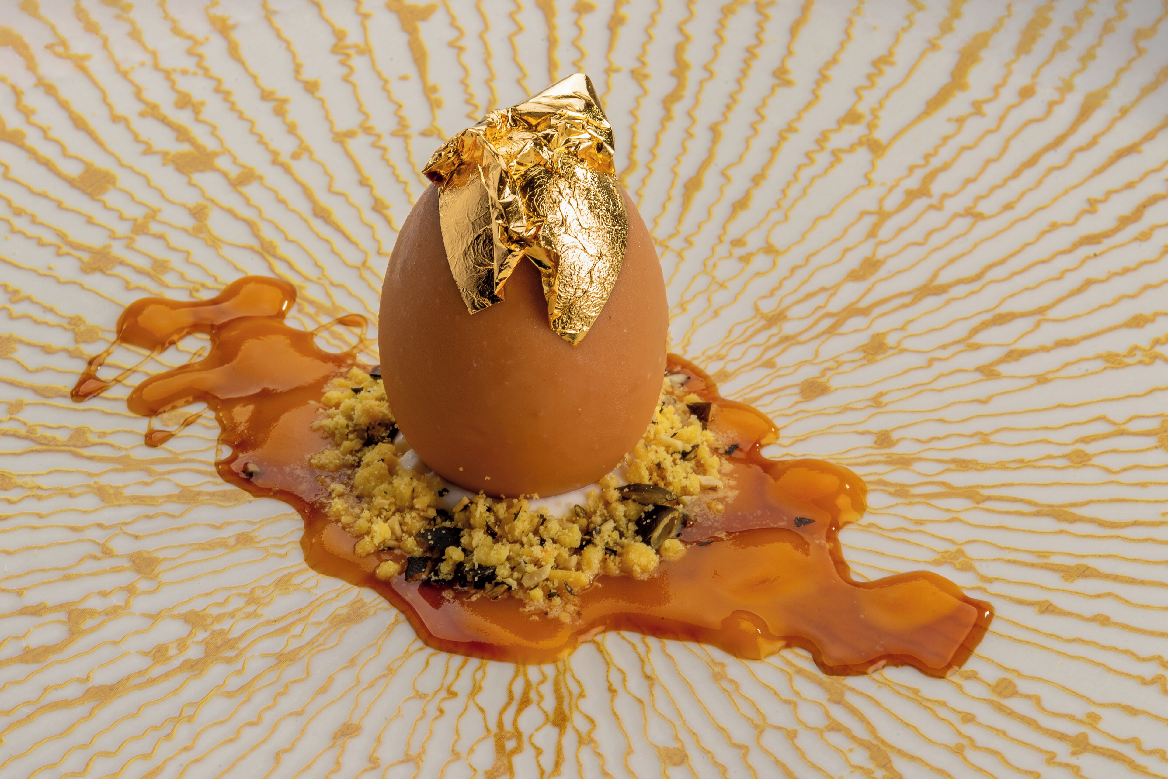 Ein Dessert mit goldenem Blatt, serviert auf einem teller mit gemustertem Dekor und Karamellsauce.