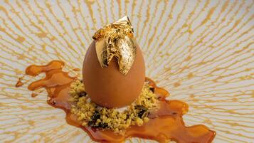 Ein Dessert mit goldenem Blatt, serviert auf einem teller mit gemustertem Dekor und Karamellsauce.