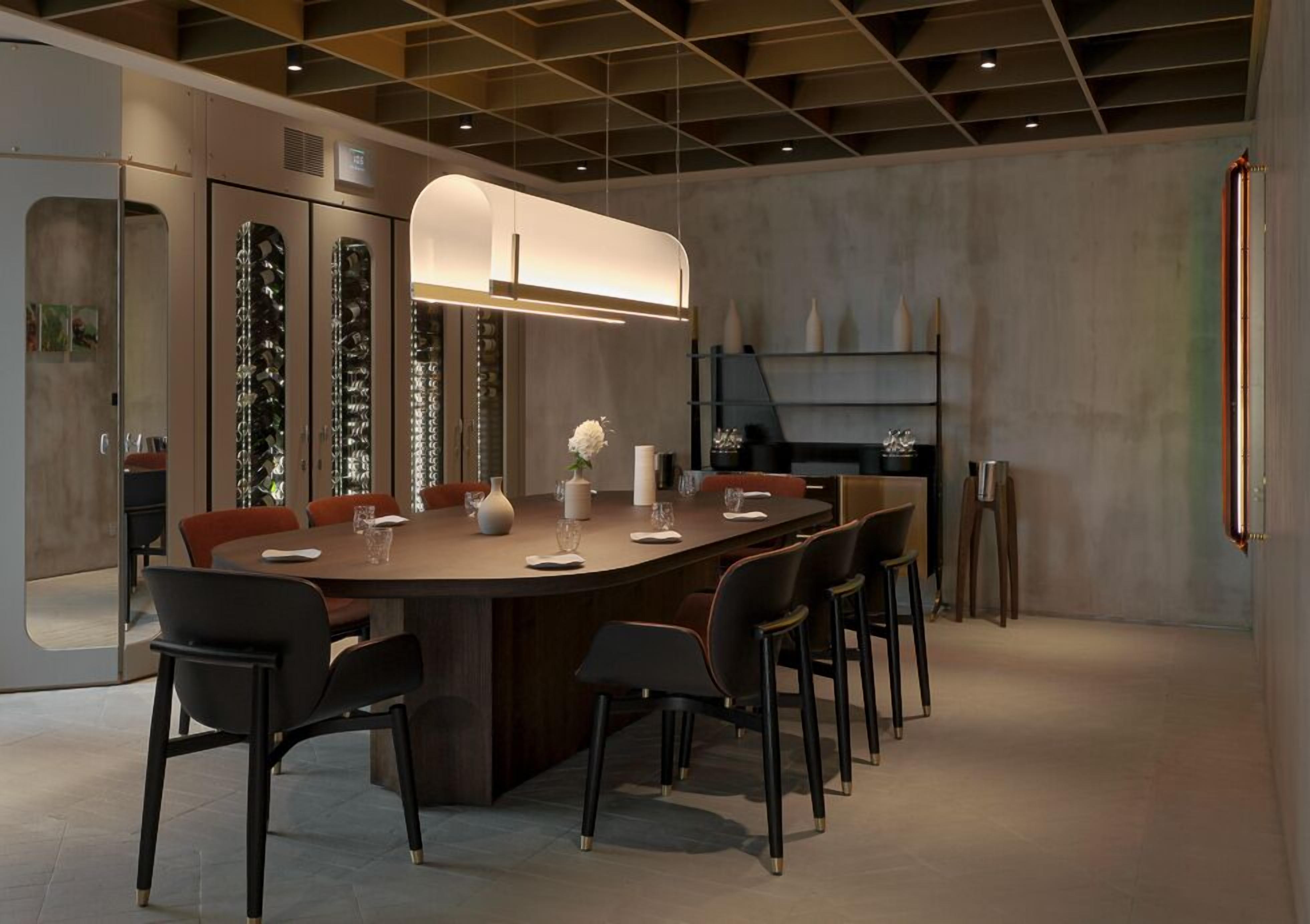 A modern dining area with a large oval table, black and red chairs, and a central light fixture.