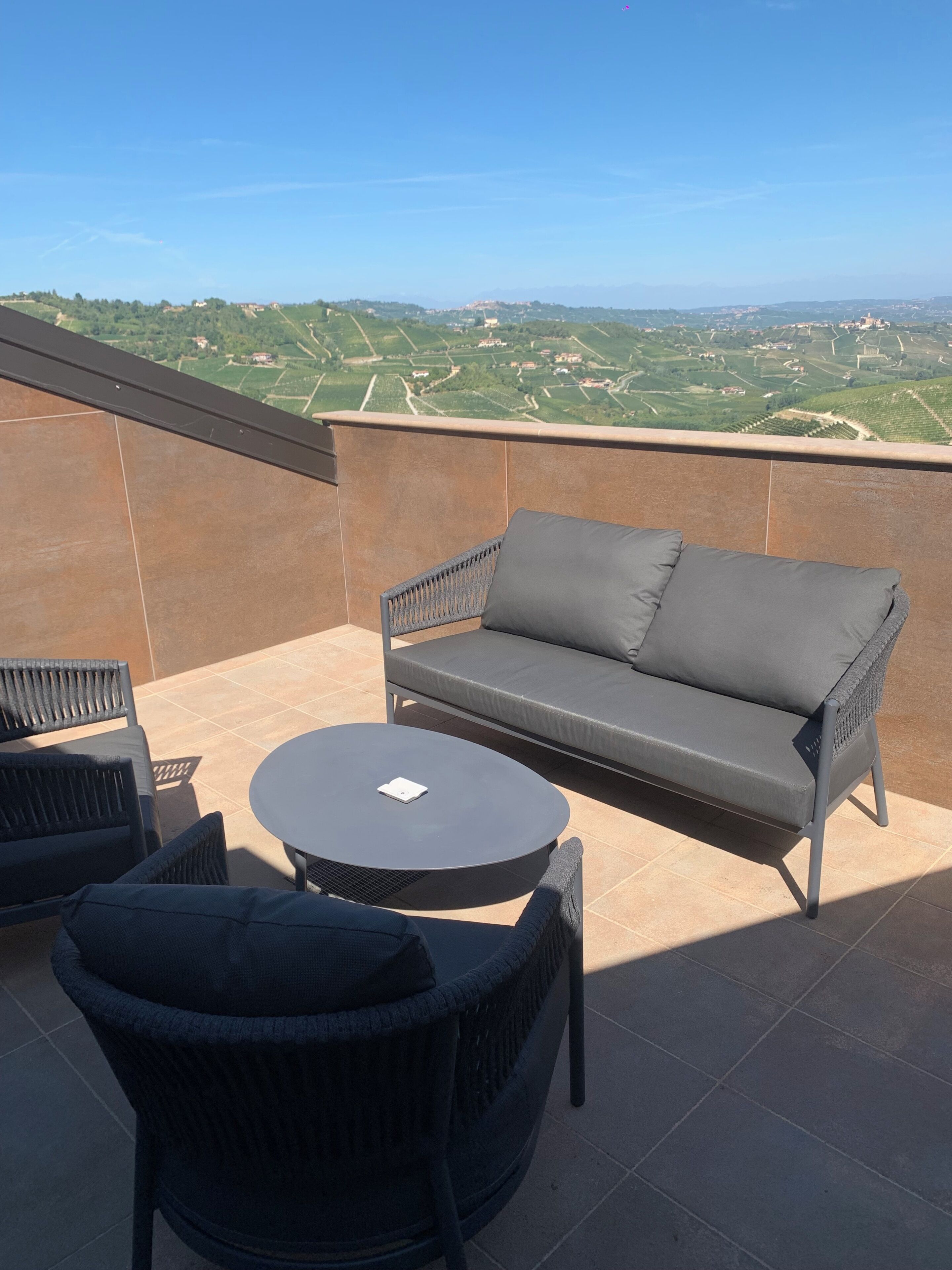 A terrace with a sofa, chairs, and a table, overlooking a scenic landscape.