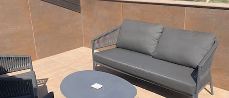 A terrace with a sofa, chairs, and a table, overlooking a scenic landscape.