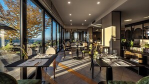 A modern restaurant with large windows, a high ceiling, and a view of the outdoors. Tables are set with white tablecloths and silverware. - Il Boscareto Resort & Spa (Serralunga d'Alba)