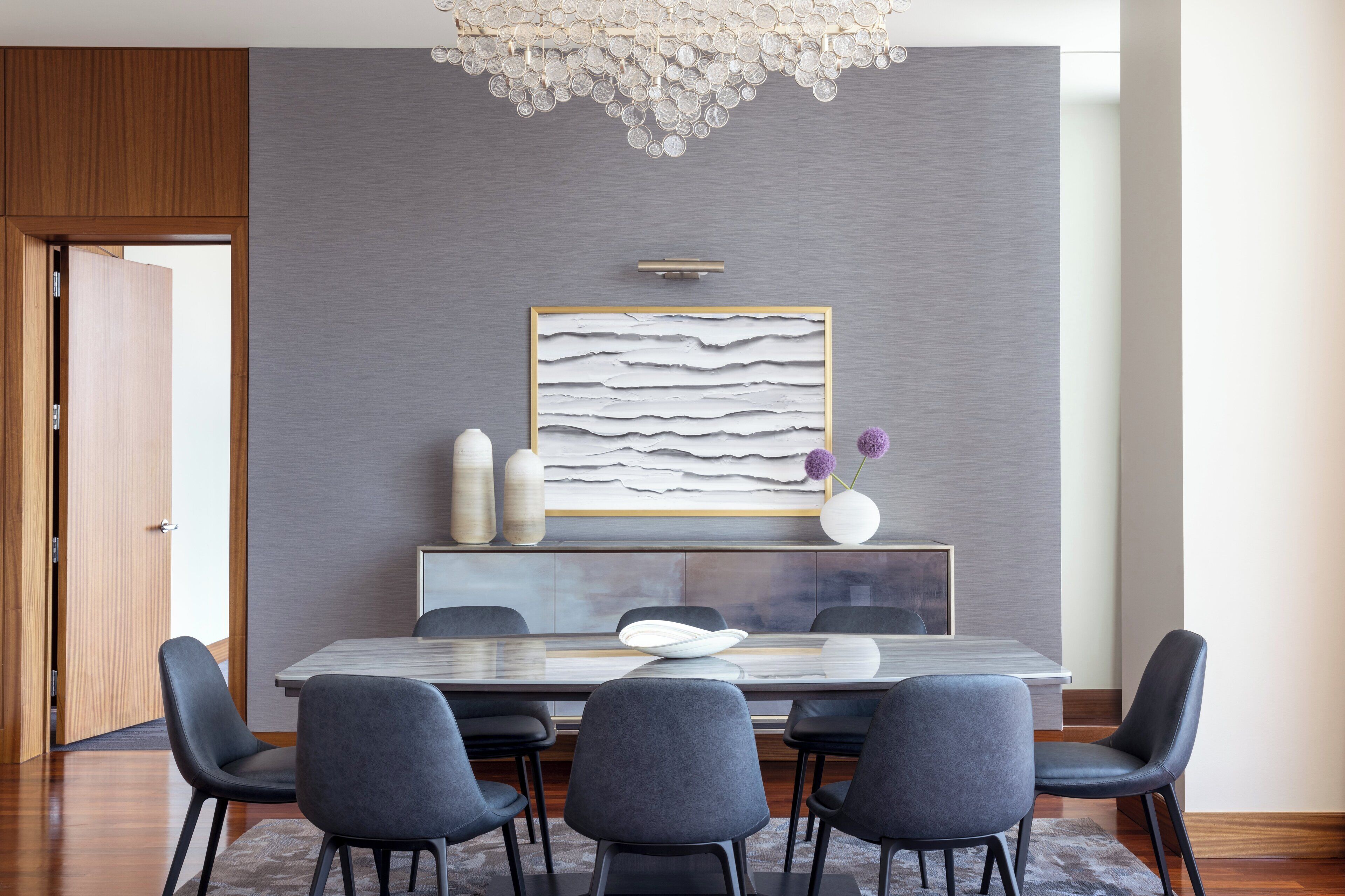Un comedor moderno con pared gris, un cuadro abstracto grande y una puerta de madera.