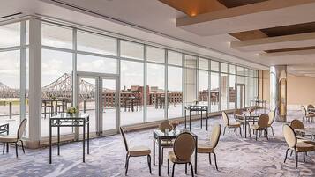 A spacious indoor area with large windows, multiple tables and chairs, and a view of a bridge and buildings outside.