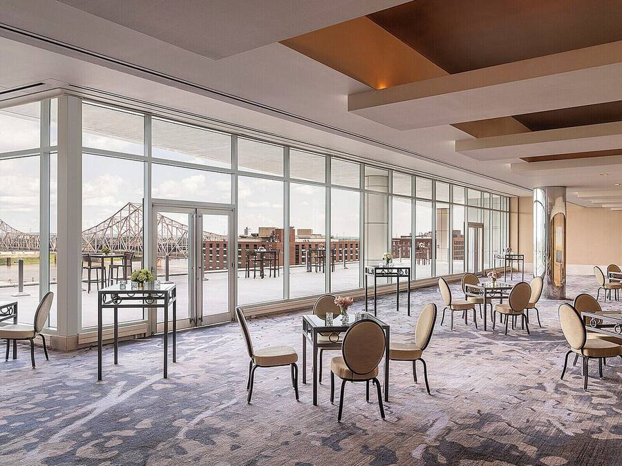 A spacious indoor area with large windows, multiple tables and chairs, and a view of a bridge and buildings outside.