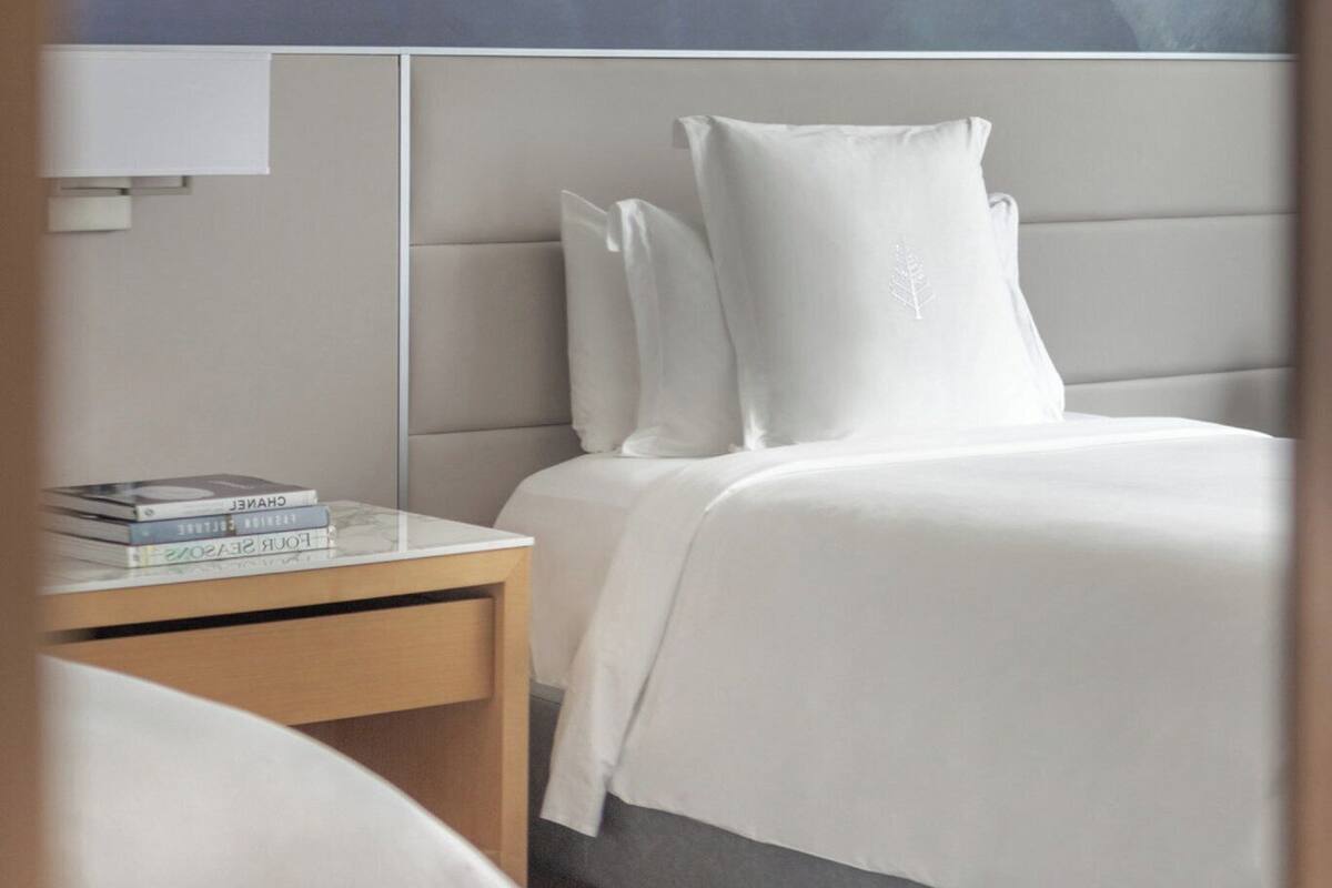 A modern hotel room with a bed, a bedside table with books, and a nightstand.