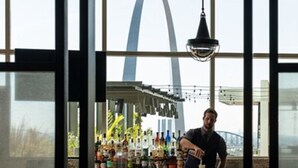 A bar area with a bartender, a bar counter with various bottles, and a view of the Gateway Arch.