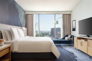 A hotel room with a large bed, a TV, a desk, and a view of the cityscape. - Four Seasons Hotel St Louis (St. Louis)