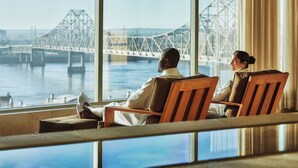 A couple relaxing by a window overlooking a bridge and water.