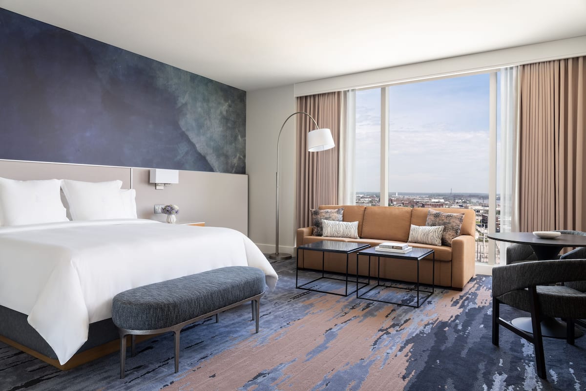 A hotel room with a large bed, a sofa, a coffee table, and a view of the city.