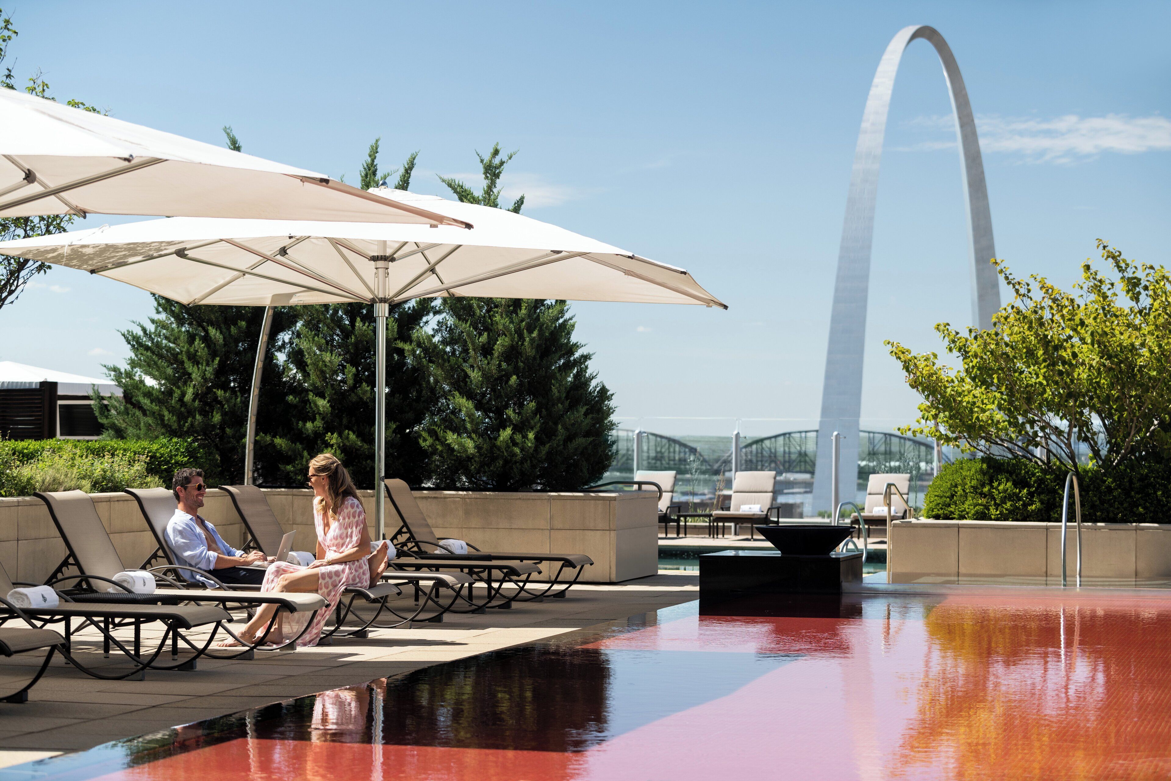 A poolside area with lounge chairs and umbrellas, a view of the Gateway Arch in the background.