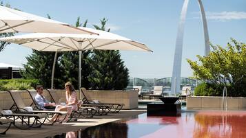 A poolside area with lounge chairs and umbrellas, a view of the Gateway Arch in the background.