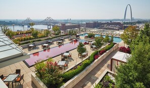 A rooftop pool area with multiple seating areas and a view of a cityscape including bridges and a distinctive arch structure. - Four Seasons Hotel St Louis (St. Louis)