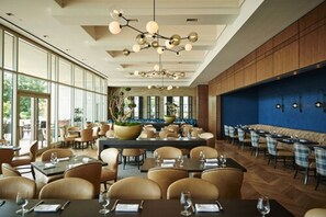 A spacious restaurant with high ceilings, modern chandeliers, and a mix of seating arrangements including tables and booths. - Four Seasons Hotel St Louis (St. Louis)