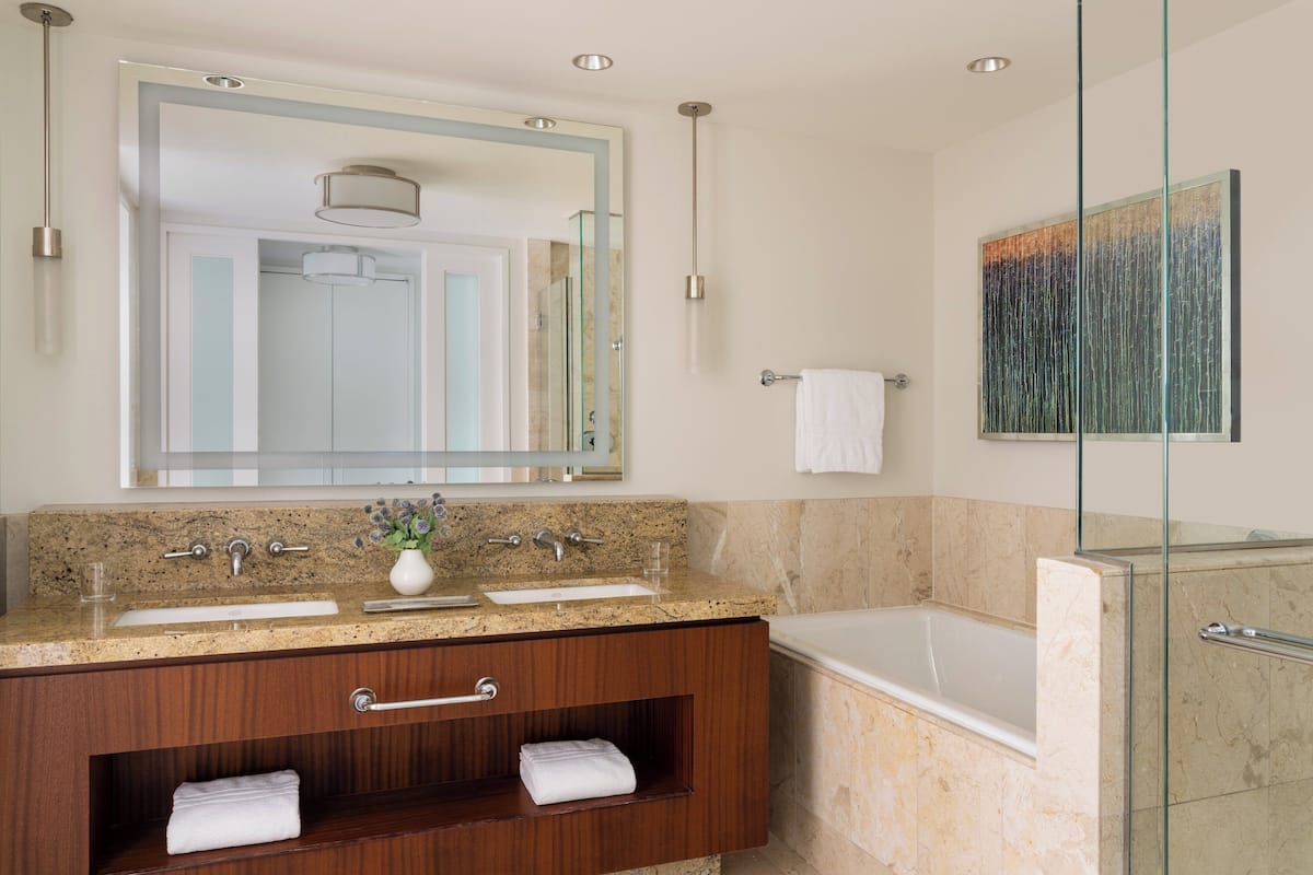 A modern bathroom with a granite countertop, a large mirror, a glass-enclosed shower, and a wooden vanity.