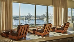A room with large windows overlooking a bridge and water, featuring wooden chairs and a small table.