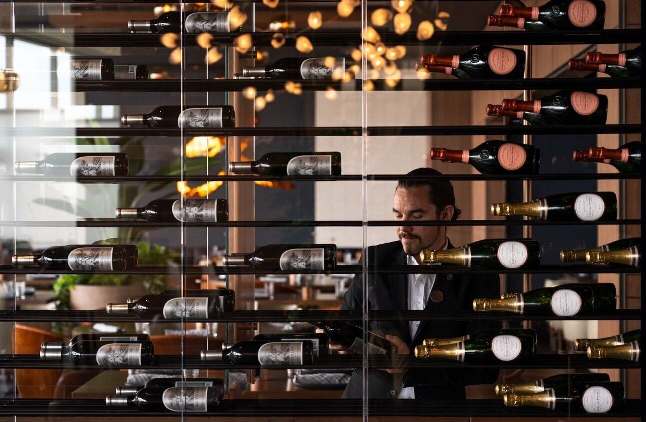 A wine rack with multiple bottles, a person in a suit, and a modern interior with hanging lights.