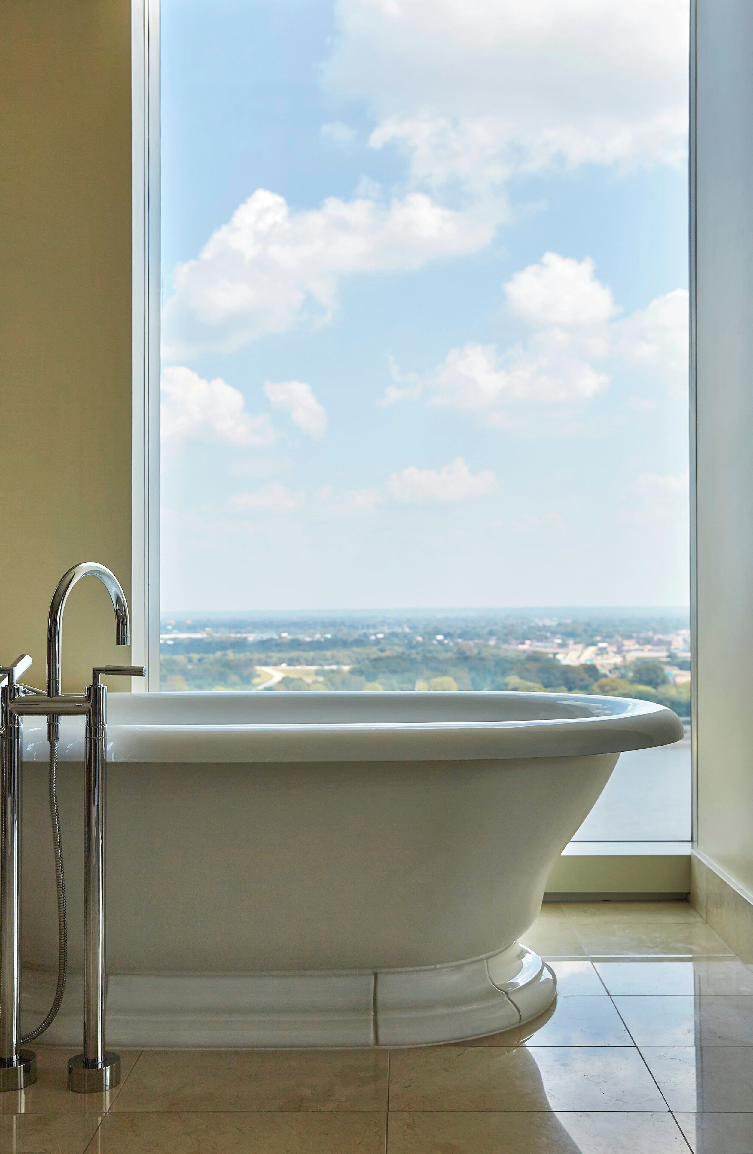 A freestanding bathtub in a bathroom with a large window offering a view of a cityscape.