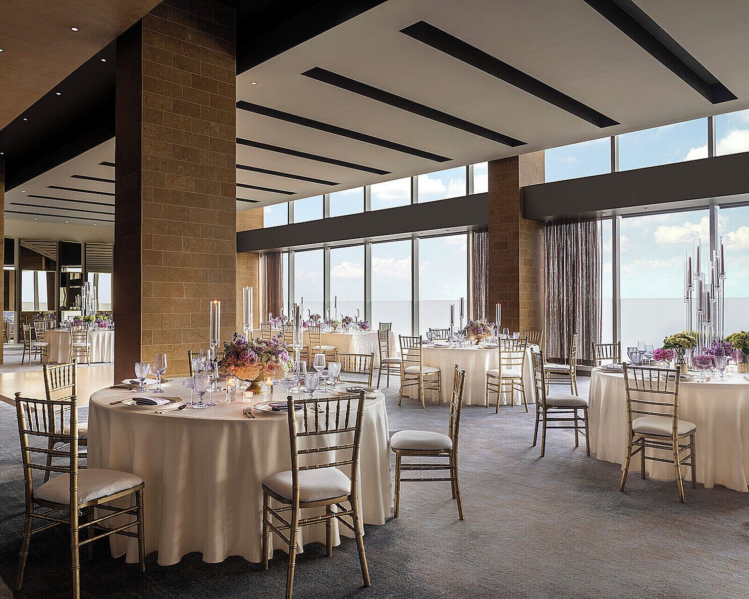 A spacious dining area with round tables, chairs, and a view of the sky through large windows.