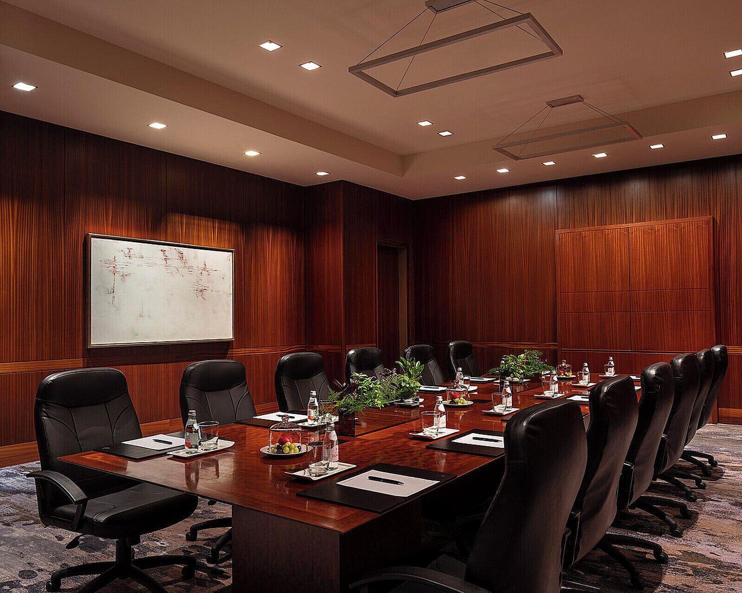 A conference room with a long wooden table, black leather chairs, and a projector screen on the wall.