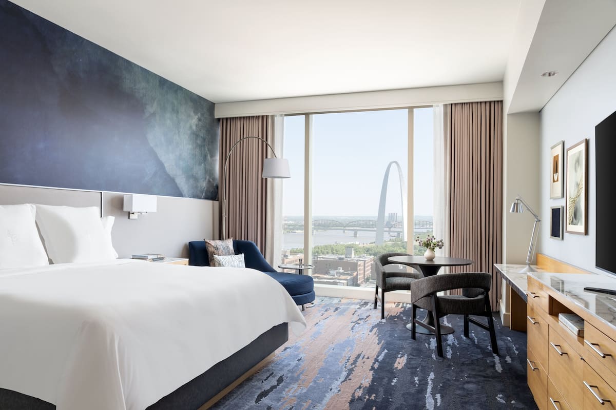 A modern hotel room with a large bed, a desk, and a view of a bridge.