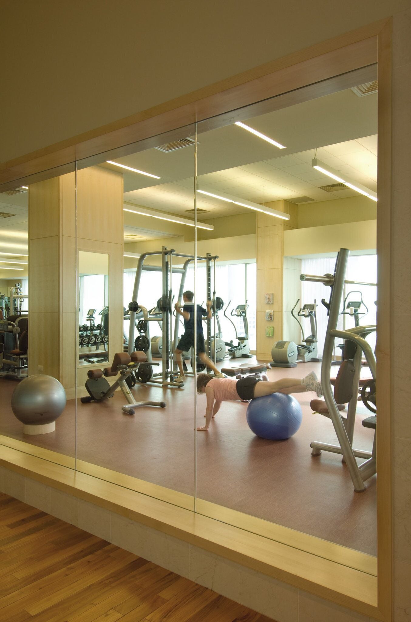 Ein Fitnessraum mit Trainingsgeräten, einem Spiegel und Holzboden.