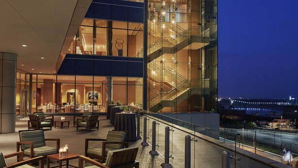 A modern hotel lobby with a glass facade, seating area, and a staircase.