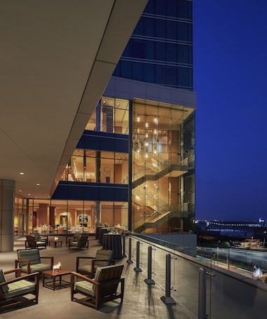 A modern hotel lobby with a glass facade, seating area, and a staircase.
