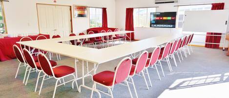 Une salle de conférence avec une longue table et des chaises rouges, un tableau blanc et un écran de projection.