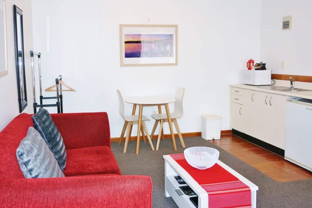 A compact living space with a red sofa, a small dining table, and a kitchenette.