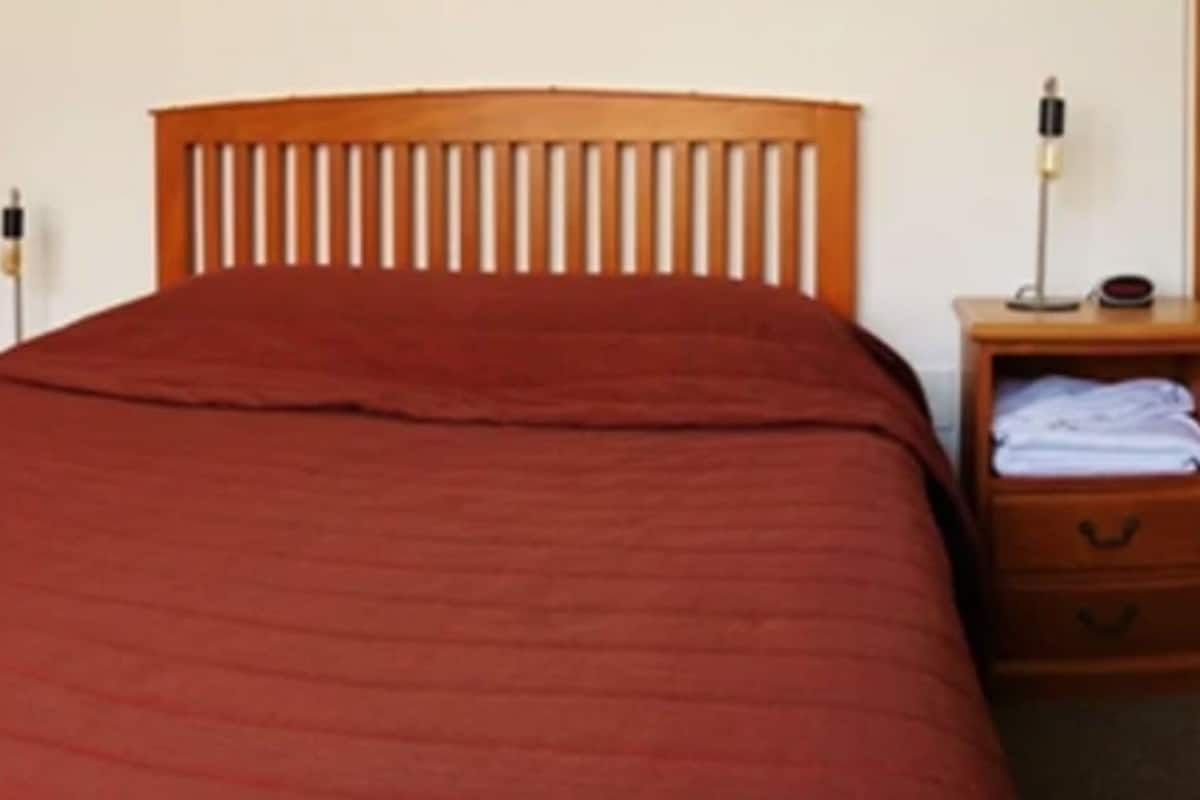 Two single beds with wooden headboards, a bedside table with a lamp, and a small drawer unit.