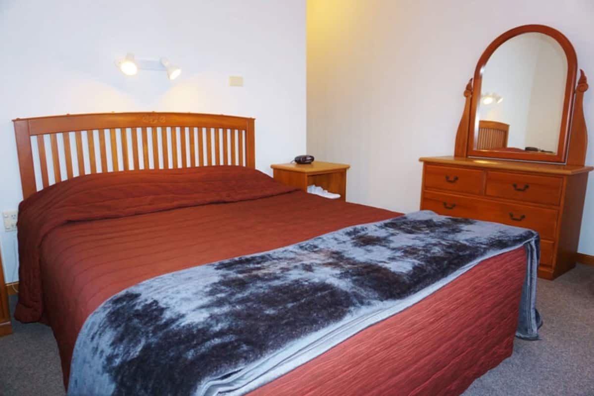A bedroom with a wooden bed, a dresser, a mirror, and a nightstand.