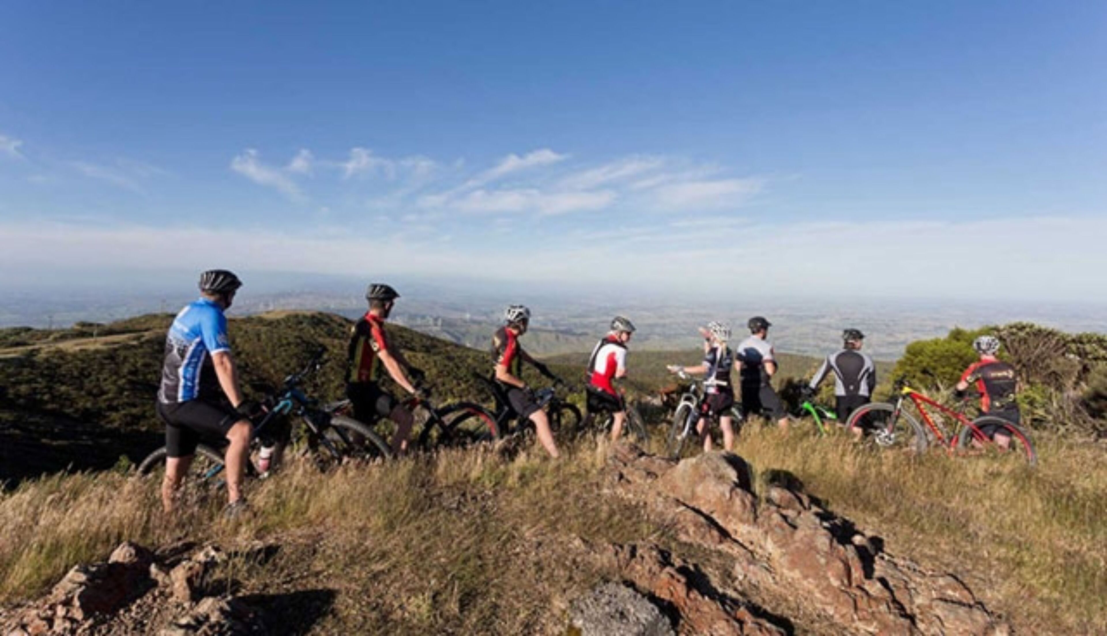 Un grupo de ciclistas de montaña en un sendero, con una vista de una ciudad al fondo.