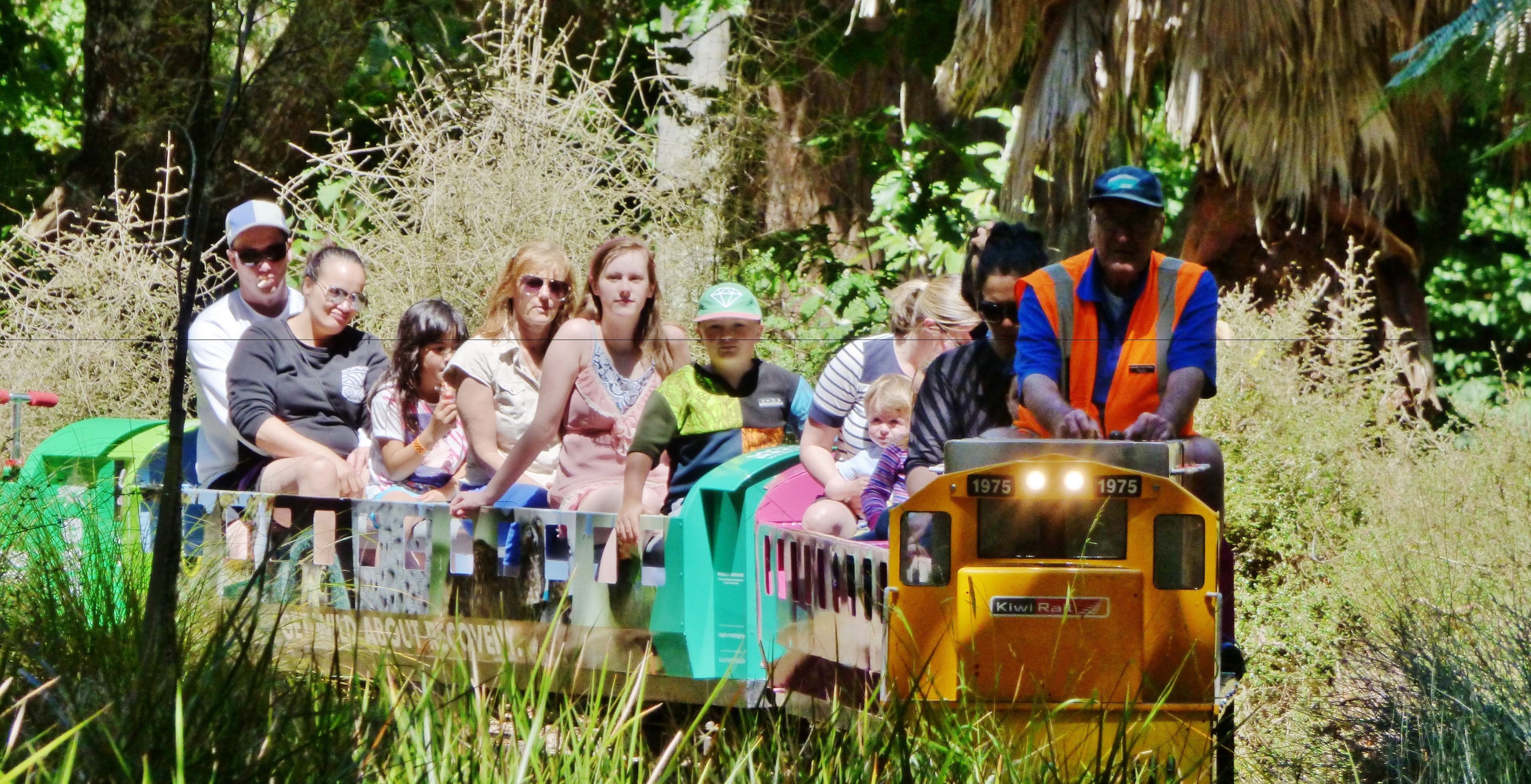 A small train with passengers, surrounded by greenery.