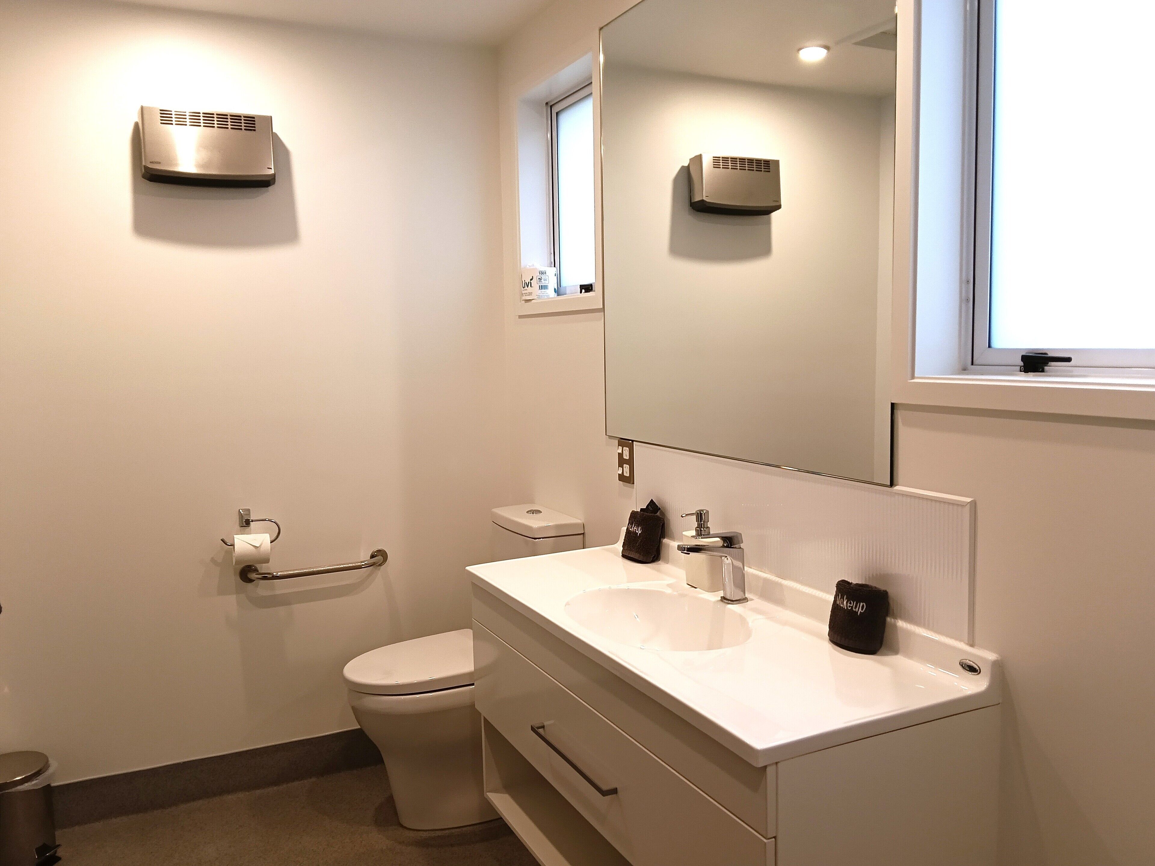Baño con inodoro, lavabo, espejo y calentador de pared.