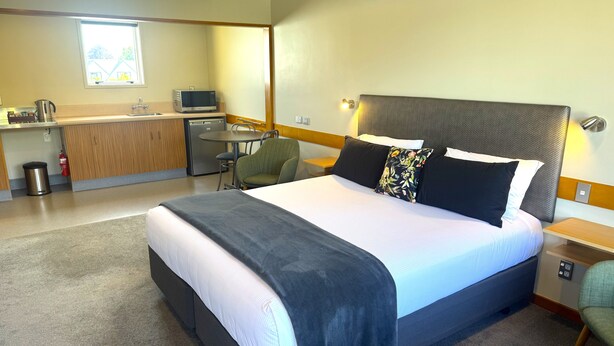 A hotel room with a bed, a desk, a chair, a small kitchenette, and a window. - Dunedin Motel and Villas (Dunedin)