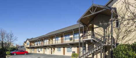 Un motel con una estructura de dos pisos, un área exterior techada y un estacionamiento.