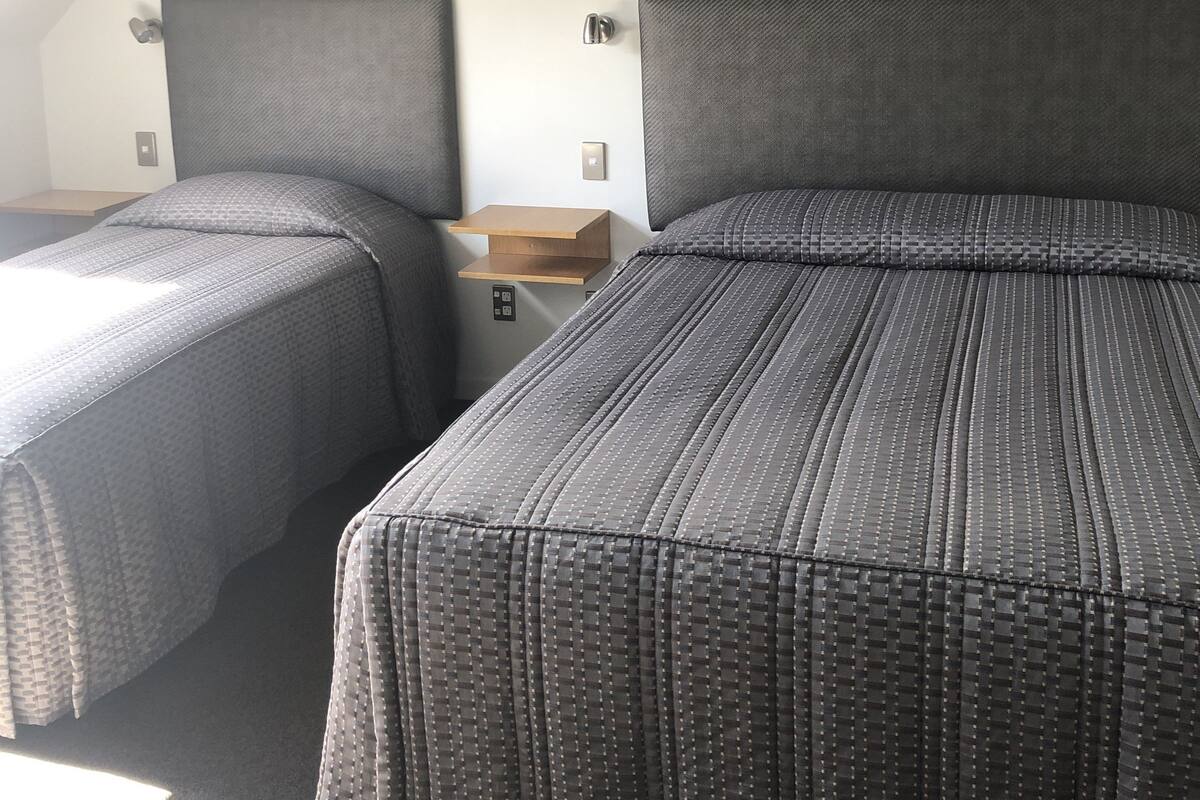A room with two beds, each with a headboard, a small wooden nightstand, and a wall-mounted light.