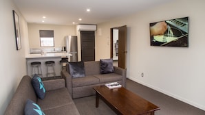 A modern living room with a sofa, coffee table, and a kitchen area in the background. - Dunedin Motel and Villas (Dunedin)
