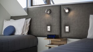 A modern bedroom with a grey headboard, a digital clock, and a small bedside table with a book. - Dunedin Motel and Villas (Dunedin)
