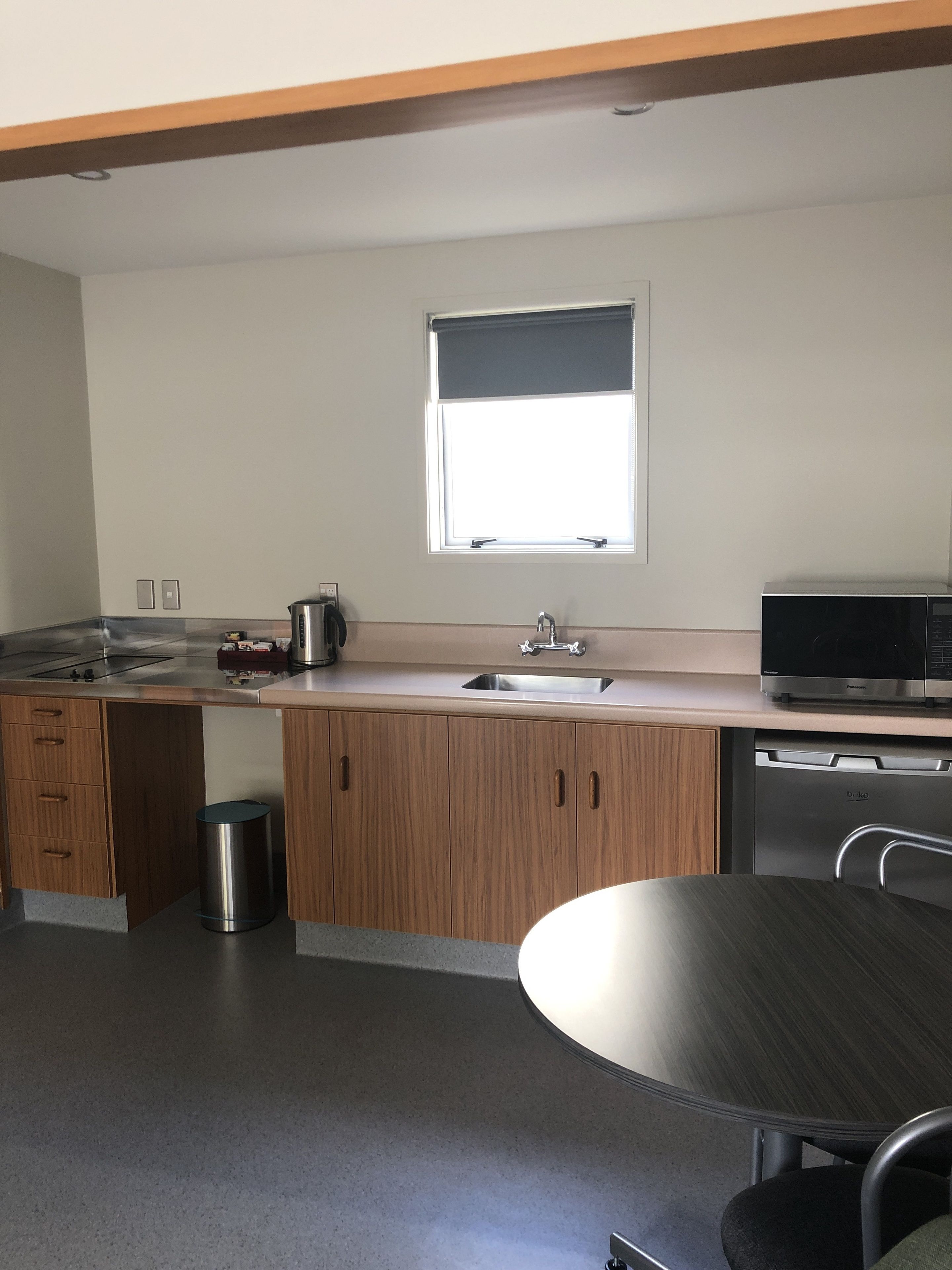 A modern kitchen with wooden cabinets, a stainless steel sink, a microwave, and a round dining table.