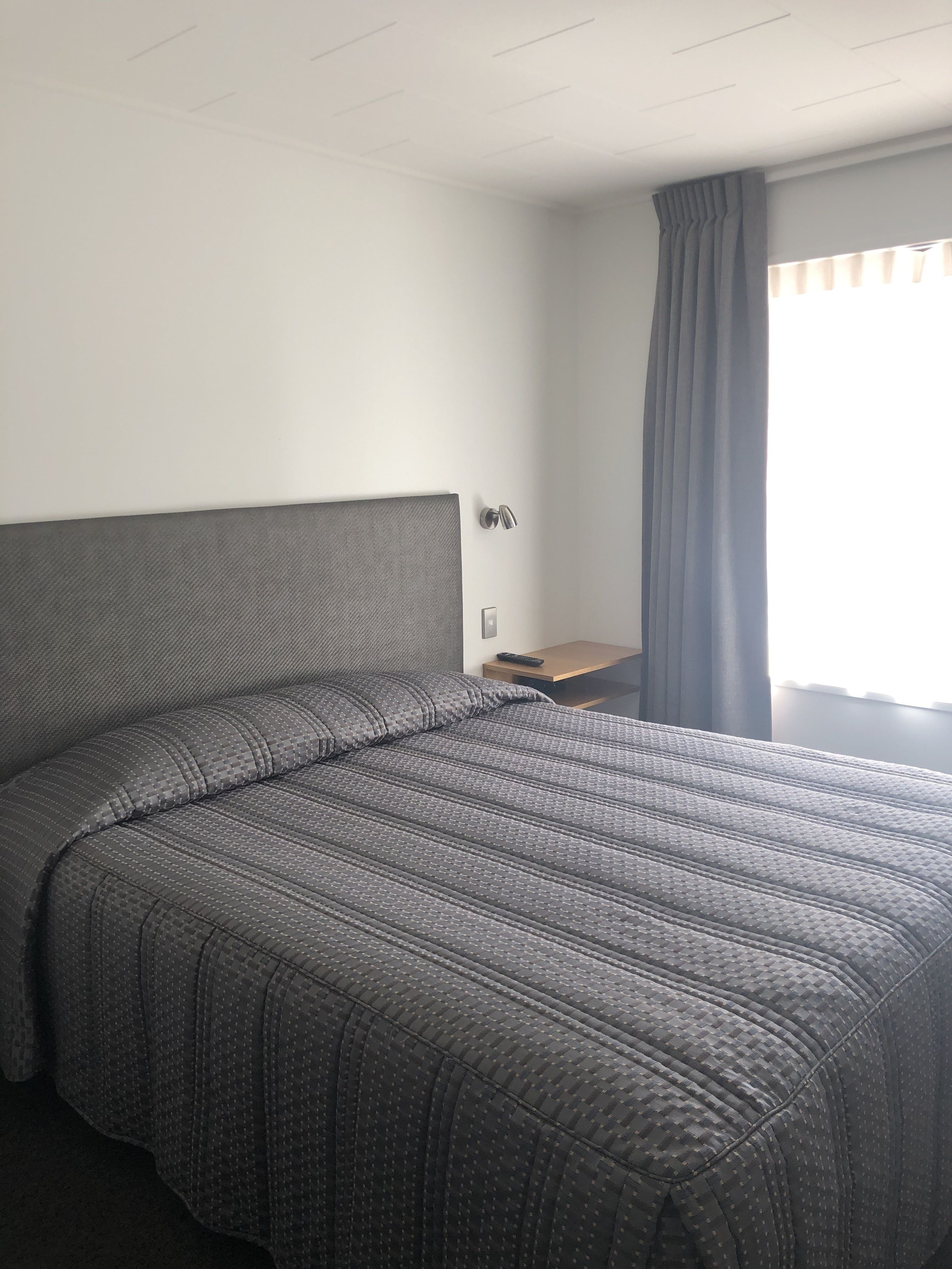 Una habitación de hotel con una cama grande, una mesita de noche, una lámpara y una ventana con cortinas.
