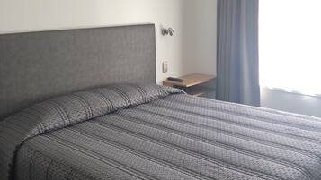 Een hotelkamer met een groot bed, een nachtkastje, een lamp en een raam met gordijnen.