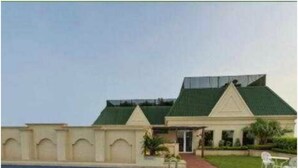 A swimming pool with a paved walkway and a building with a green roof. - Savoy Suites (Noida)