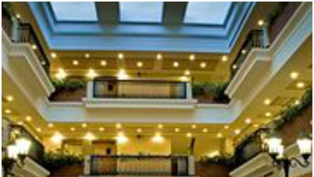 A multi-level hotel lobby with a central seating area, multiple floors, and a large windowed atrium. - Savoy Suites (Noida)