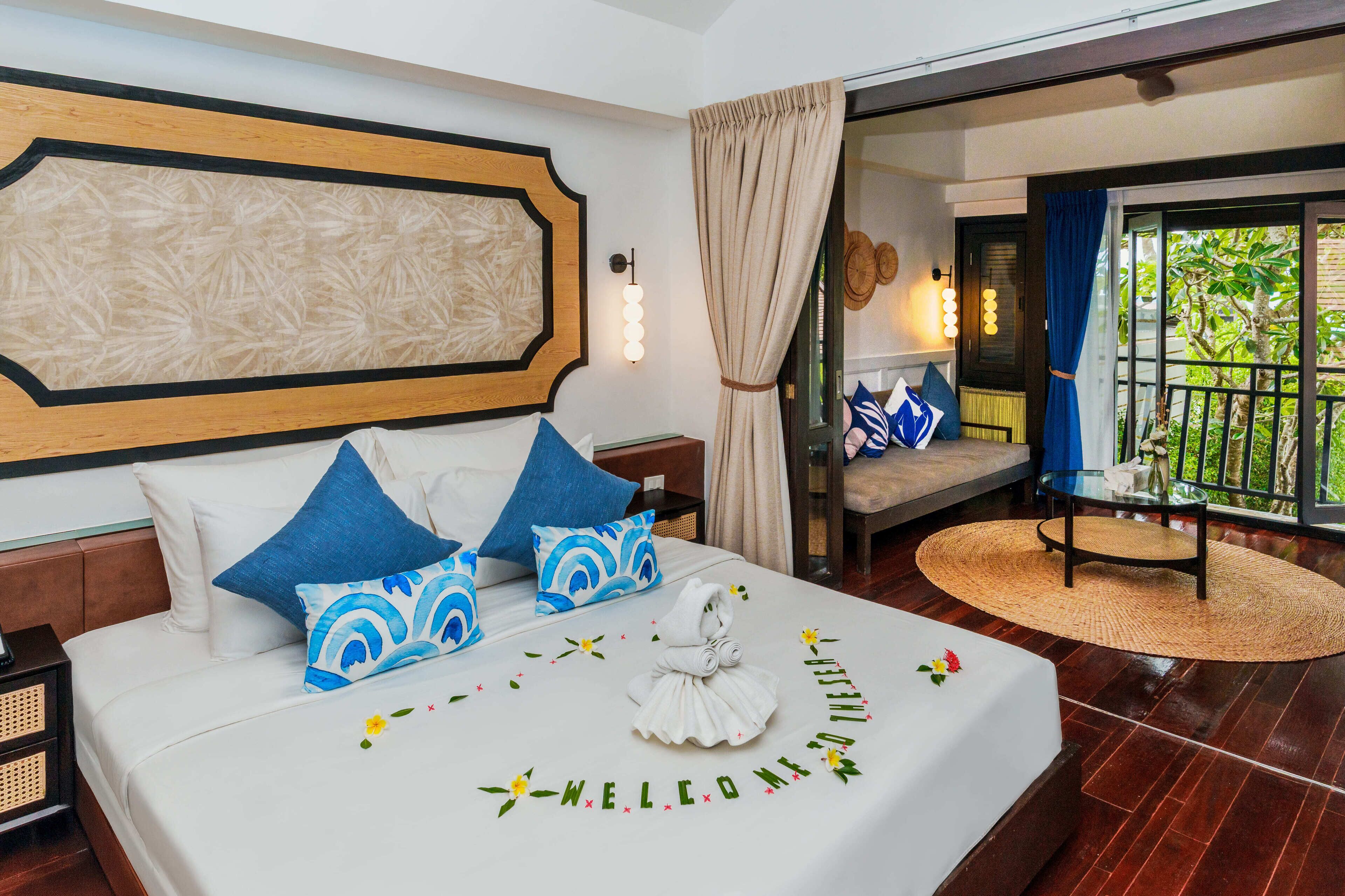 A hotel room with a bed, a nightstand, a wall-mounted light, and a view of the outdoors.