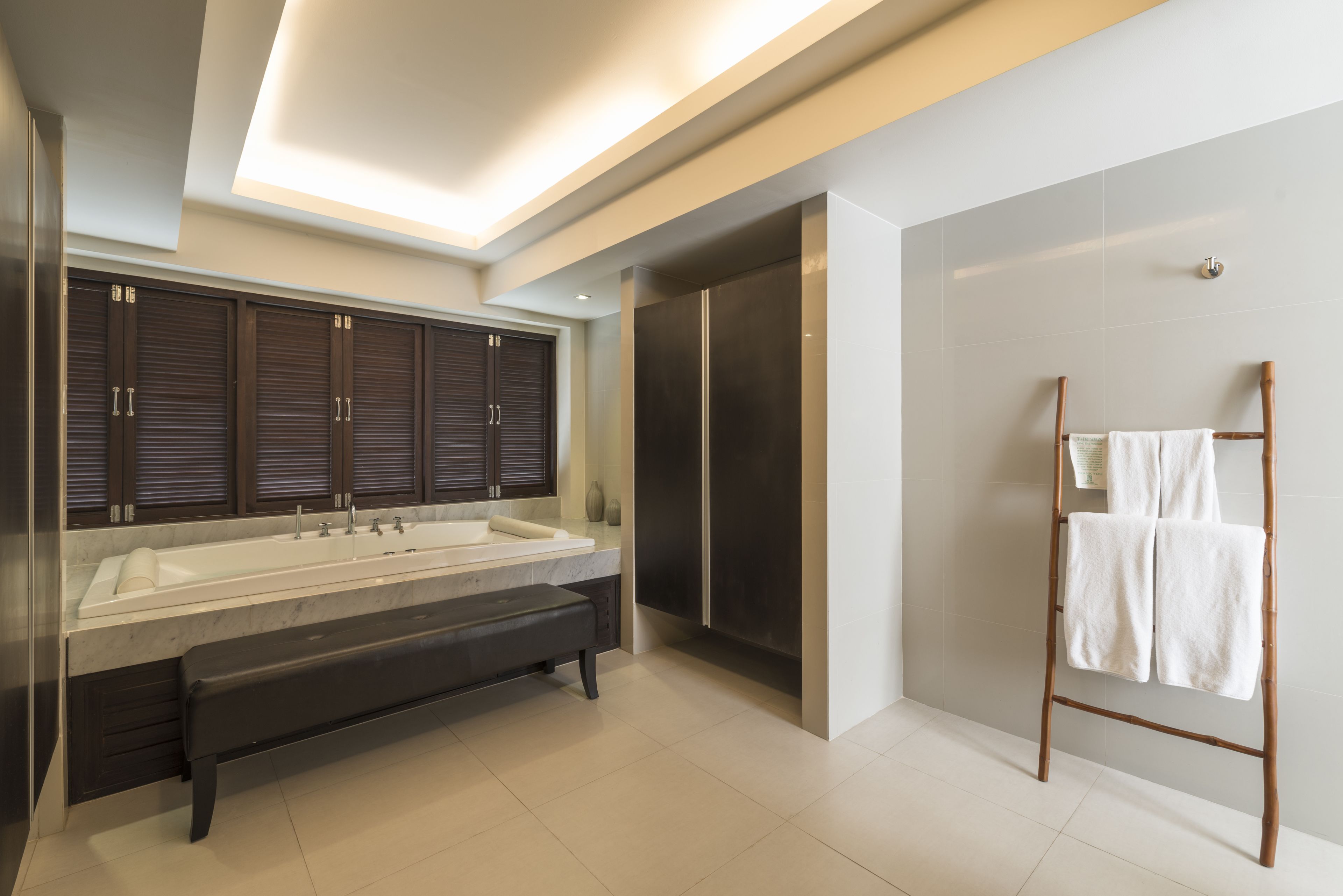 Un baño moderno con una bañera grande, un banco, cabina de ducha y un perchero de madera.